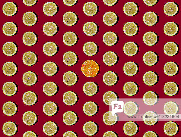 Pattern of halved lemons flat laid against red background with single tangerine in center