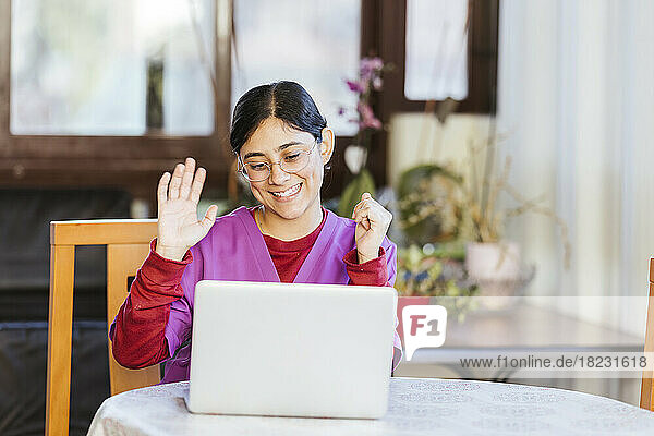 Young caregiver waving on video call through laptop at home