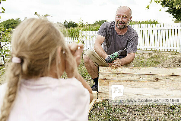 Mature father holding screwdriver talking with daughter in back yard