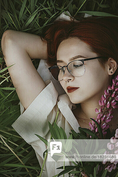 Redhead girl lying on grass with lupin flowers