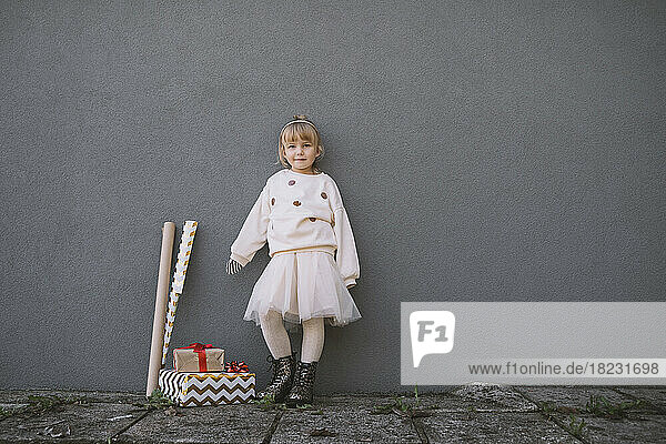 Girl leaning by wrapping paper and gift boxes on gray wall
