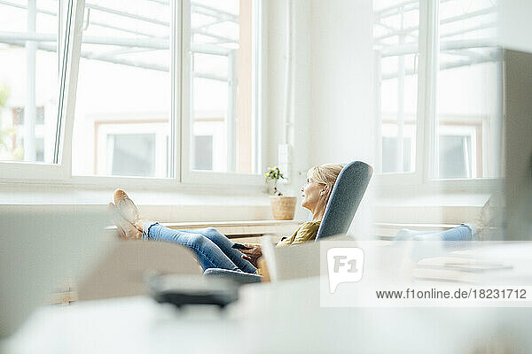 Mature businesswoman with mobile phone relaxing on armchair