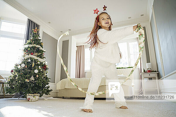 Happy girl playing with Christmas ribbon at home