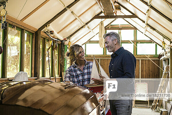 Happy man and woman discussing over model sailboat in garage