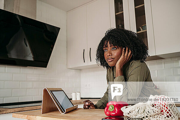 Thoughtful woman leaning on kitchen island at home