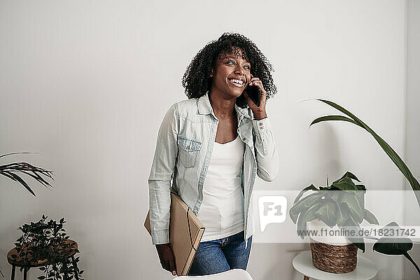 Happy businesswoman holding file talking on smart phone at home office