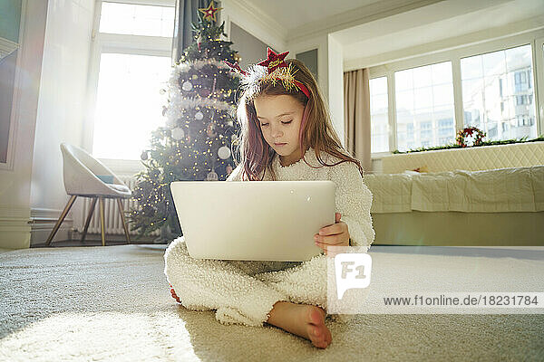 Girl with long hair using laptop sitting on carpet at home