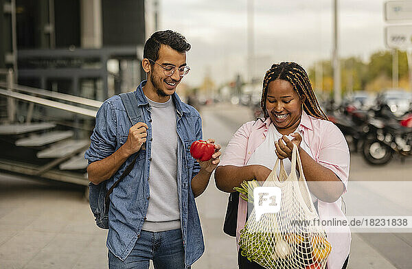 Happy young man with woman holding bag of vegetables at footpath