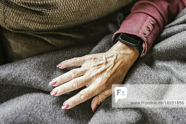 Hand of senior woman with smart watch over blanket