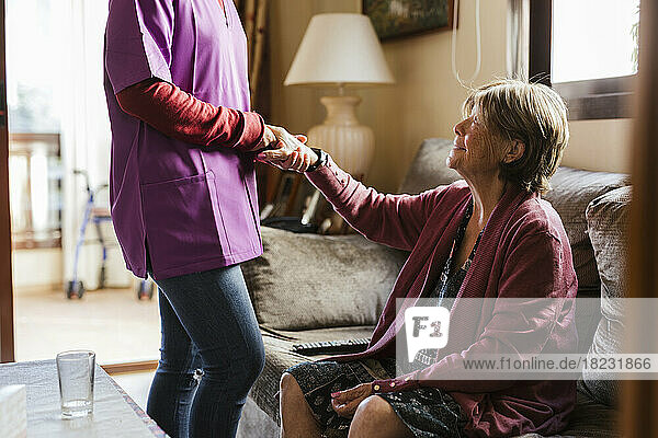 Gesundheitshelfer hält Händchen mit älterer Frau im Wohnzimmer