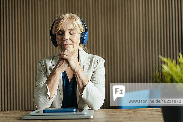 Mature businesswoman listening to music with wireless technologies on desk