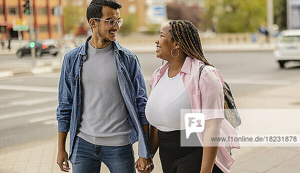 Happy young couple holding hands and walking on footpath