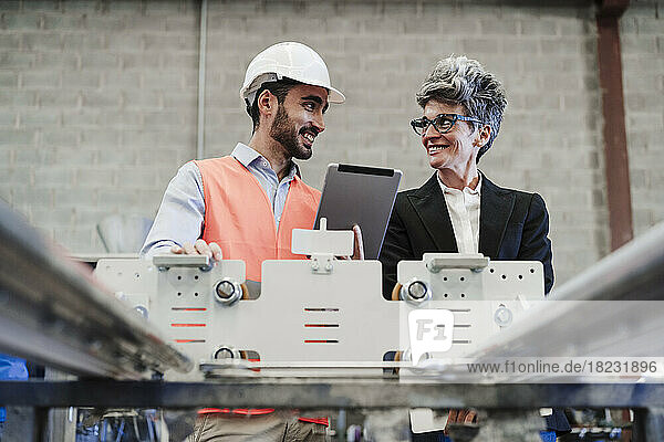 Happy businesswoman with colleague holding tablet PC standing by machine in industry