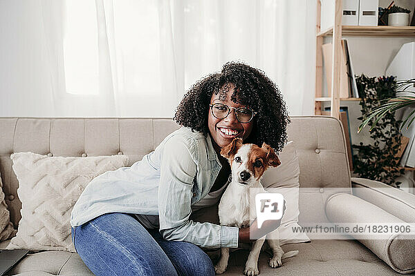 Glückliche Frau umarmt Hund  der zu Hause auf dem Sofa sitzt