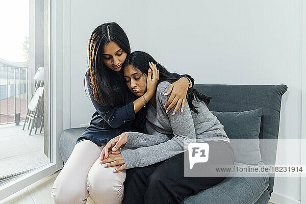 Junge Frau tröstet Schwester auf Sofa im Wohnzimmer