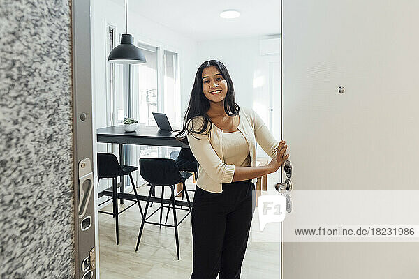 Smiling young woman opening door at home