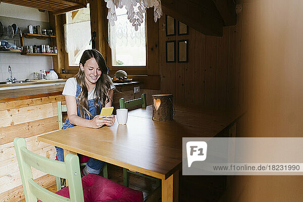 Smiling woman using smart phone at dining table in chalet