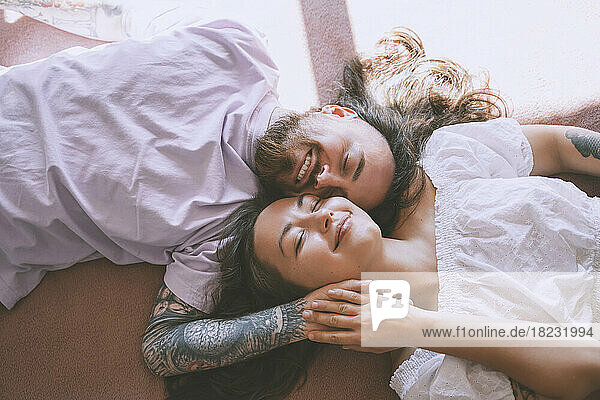 Happy romantic couple with eyes closed lying on bed at home