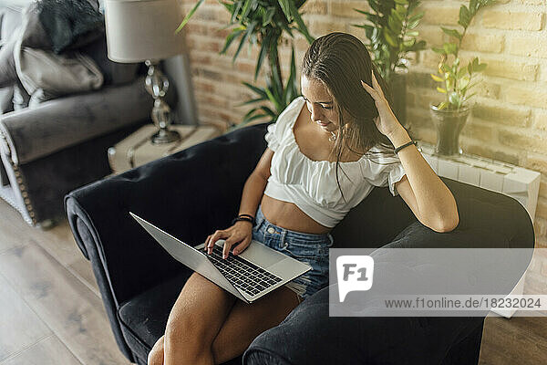 Mädchen benutzt Laptop und sitzt zu Hause auf einem Sessel