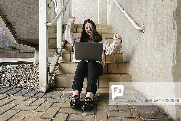 Happy young woman with laptop sitting on staircase