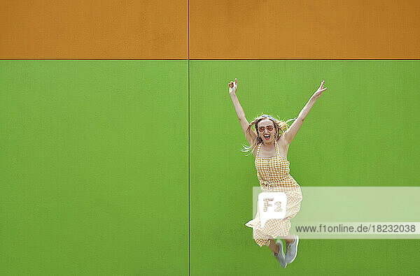 Cheerful woman jumping in front of green wall