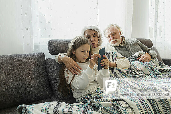 Großeltern und Enkelin sitzen auf der Couch unter einer Decke