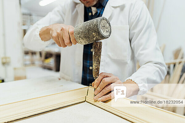 Hände eines Handwerkers  der in der Werkstatt ein Arbeitsgerät zur Herstellung eines Rahmens verwendet