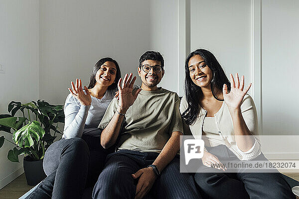 Smiling women and man waving hands sitting on sofa in living room