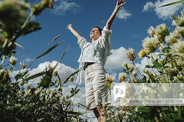 Carefree woman amidst wildflowers standing under sky