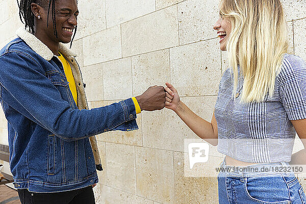 Friends giving fist bump together standing in front of wall