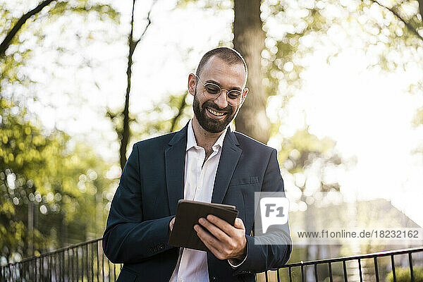 Happy businessman using tablet PC by railing