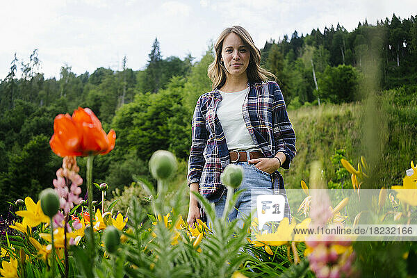 Lächelnde Frau  die inmitten von Blumen auf dem Feld steht