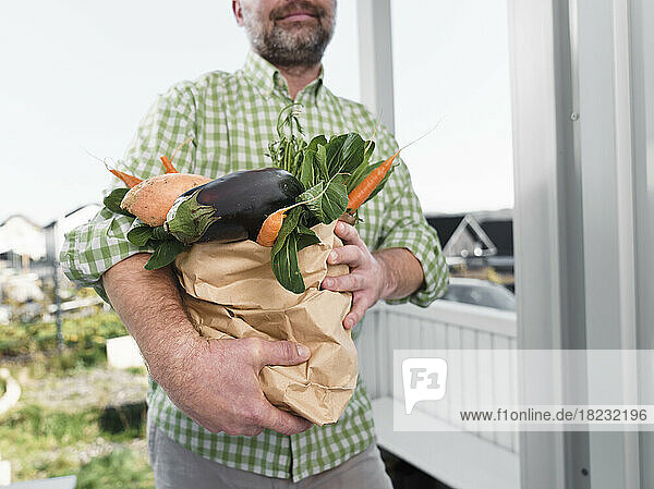Man carrying vegetables in paper bag at doorway