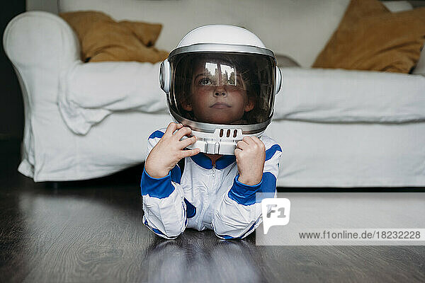 Nachdenkliches Mädchen im Weltraumkostüm und Helm liegt zu Hause auf dem Boden