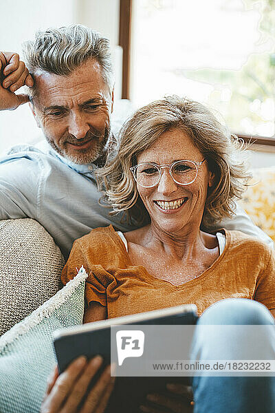 Happy woman wearing eyeglasses using tablet PC with man at home