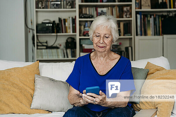 Smiling senior woman using smart phone on sofa in living room