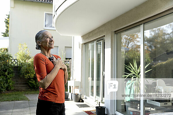 Happy senior woman with mobile phone looking at house