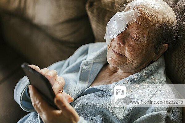 Injured senior woman using smart phone on sofa at home