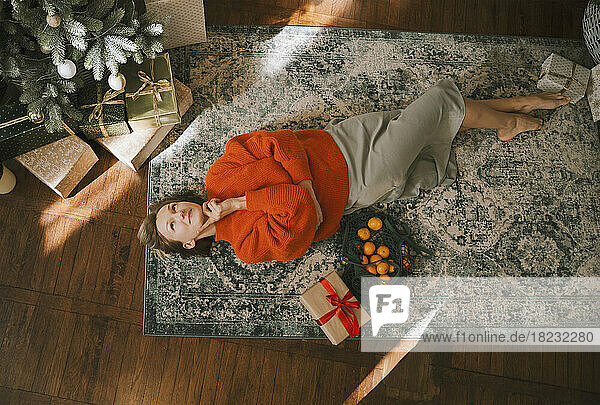 Contemplative woman lying on carpet at home