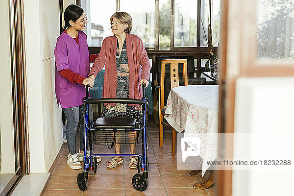 Smiling caregiver helping senior woman to walk with mobility walker at home