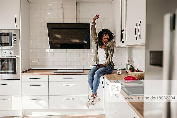 Frau mit erhobener Hand sitzt zu Hause auf der Küchentheke