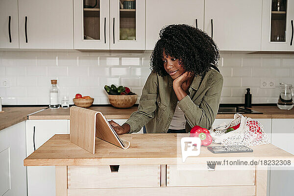 Woman with hand on chin using tablet PC at kitchen