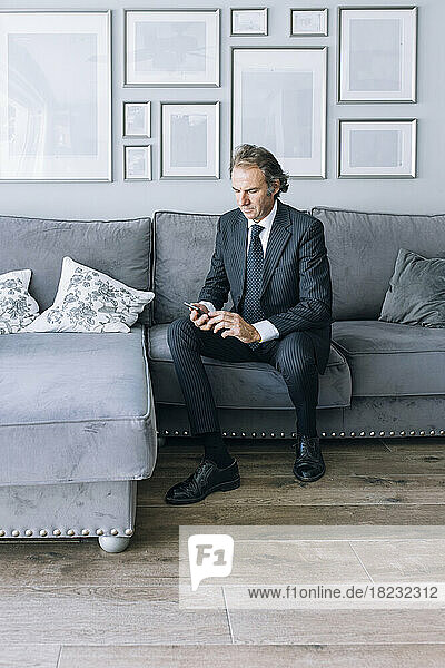 Mature businessman using smart phone on sofa at home