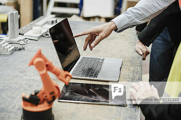 Hand of businessman pointing on laptops screen with colleagues at industry