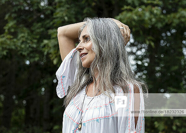 Smiling gray haired woman with arm raised at forest