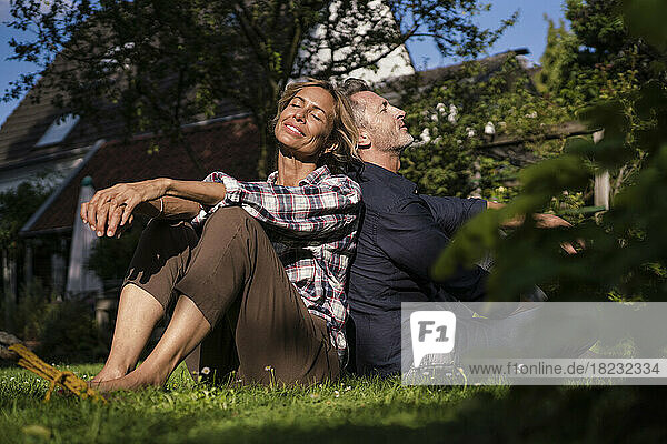Happy mature man and woman sitting together on grass in backyard