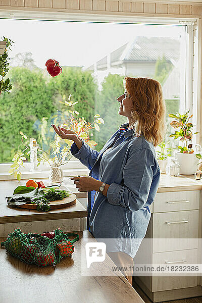 Woman in kitchen throwing fresh red pepper