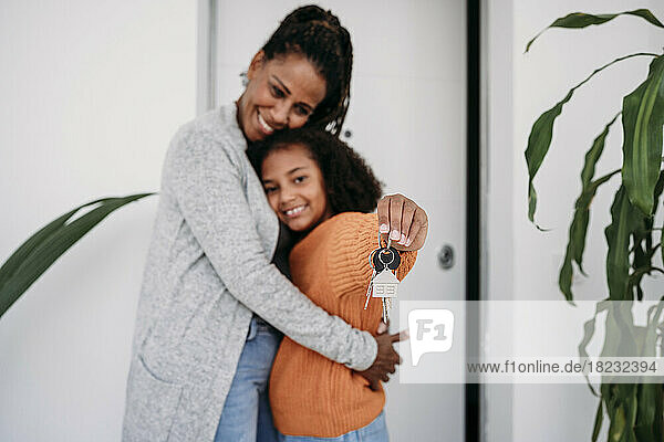 Glückliche reife Frau umarmt Tochter und zeigt Hausschlüssel