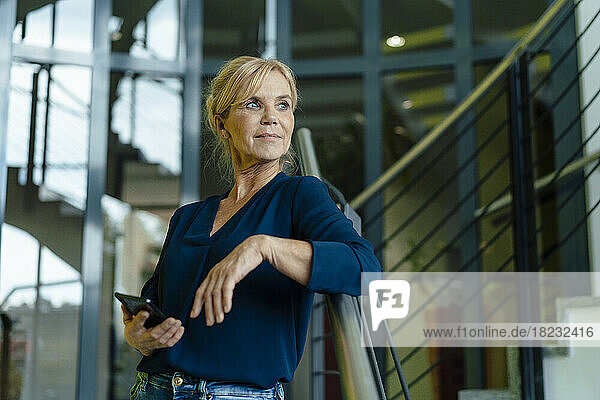 Contemplative businesswoman holding mobile phone on staircase