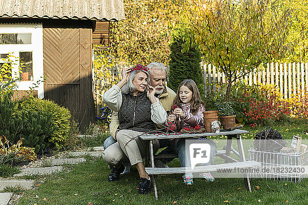 Grandparents and granddaughter sitting at garden table crafting with mountain ash